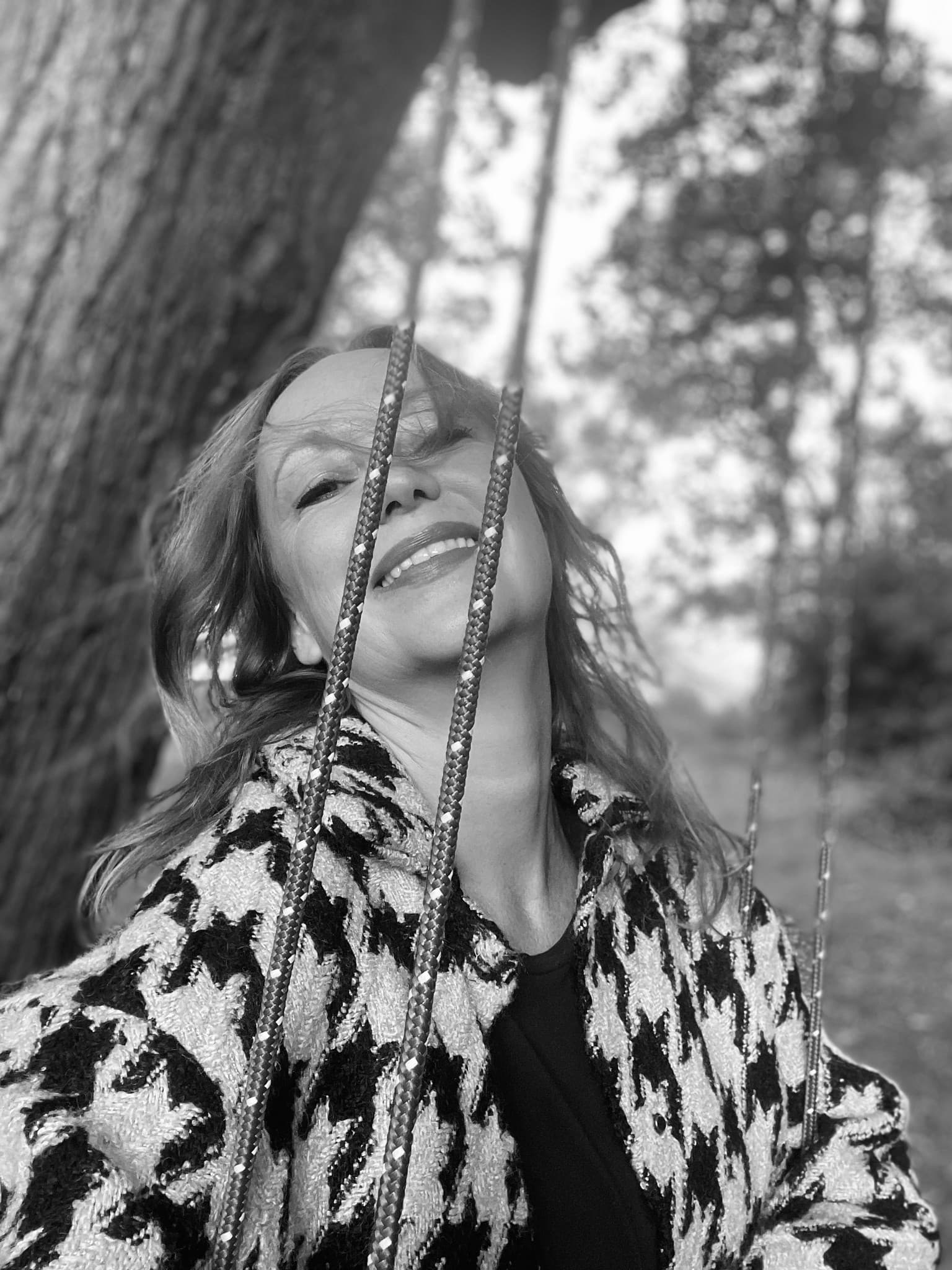 Schwarz-Weiß-Foto: Anja Wolfram auf einer Schaukel im Wald, den Kopf zurückgelehnt