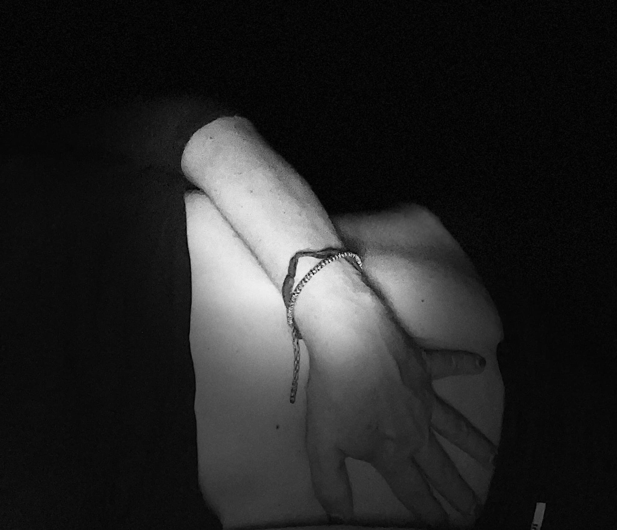 Schwarz-Weiß-Foto: eine Hand mit Armband ruht auf einem Knie