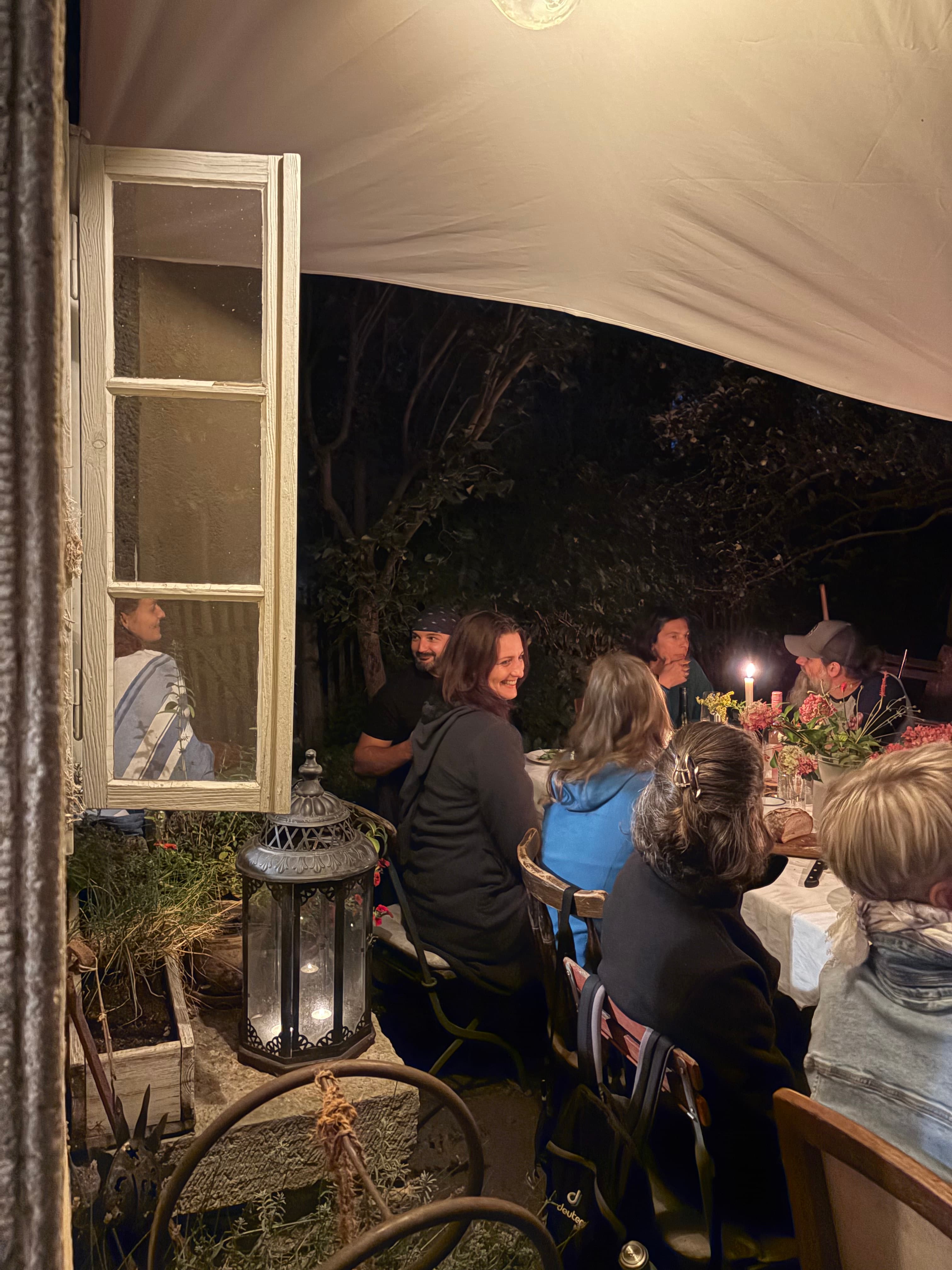 Gruppe an einer langen Tafel im Garten, Laternen- und Kerzenlicht am Abend