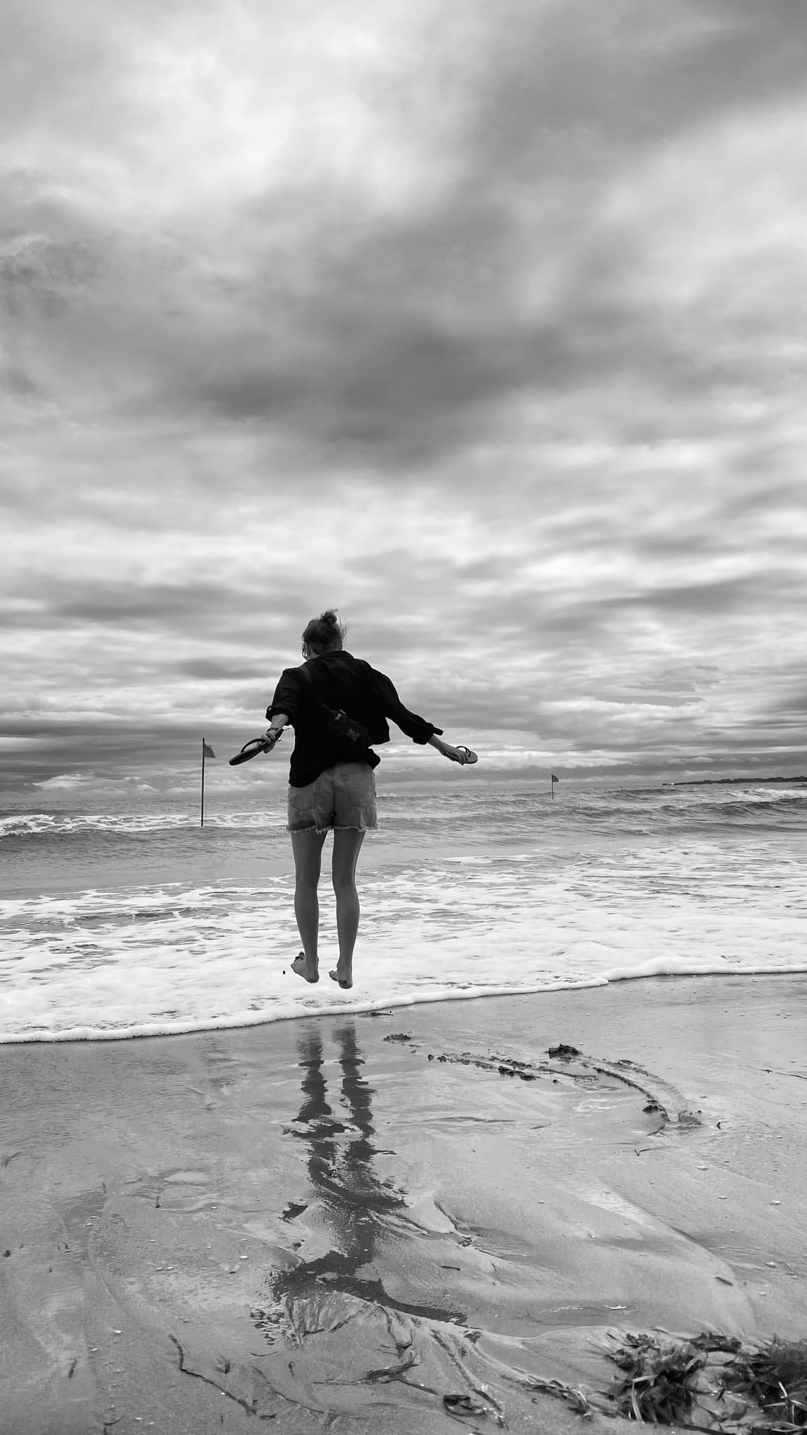 Schwarz-Weiß-Foto: eine Person springt am Strand in die Luft